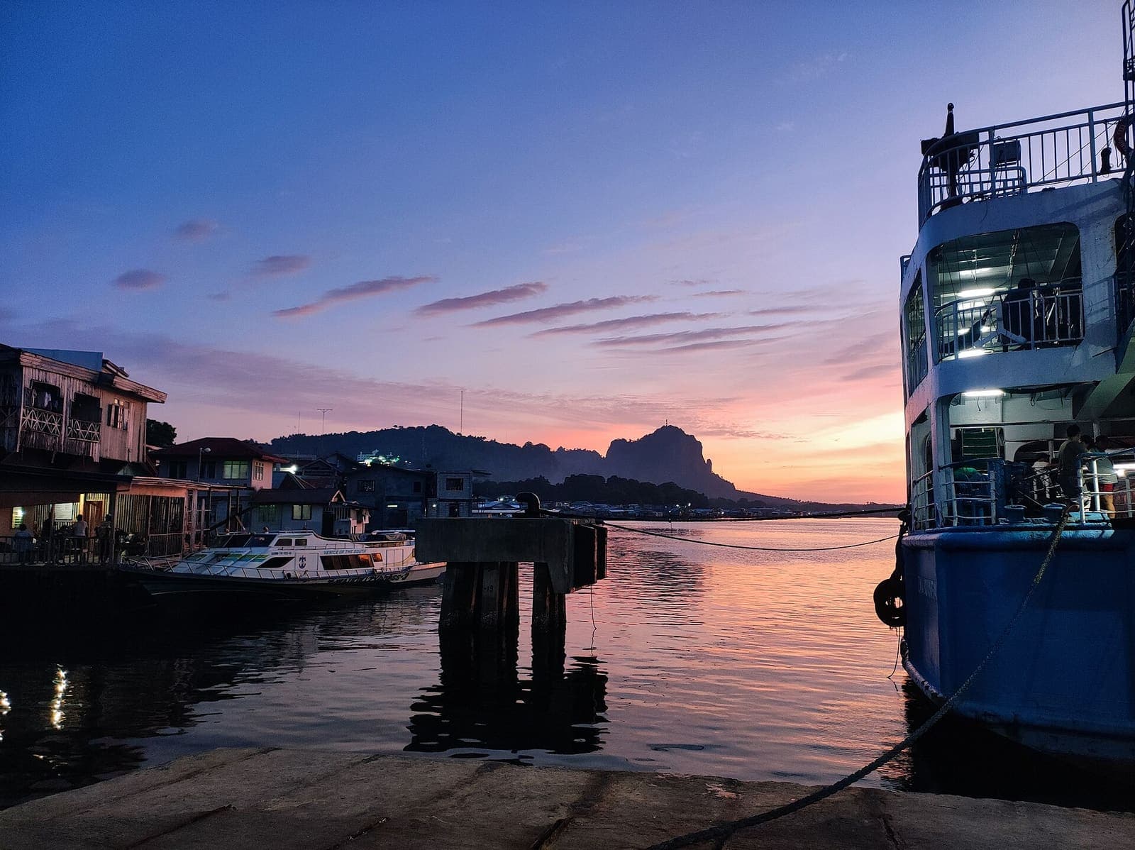 Bud Bongao rising behind a harbour at dusk, boats moored under a pink and violet sky.